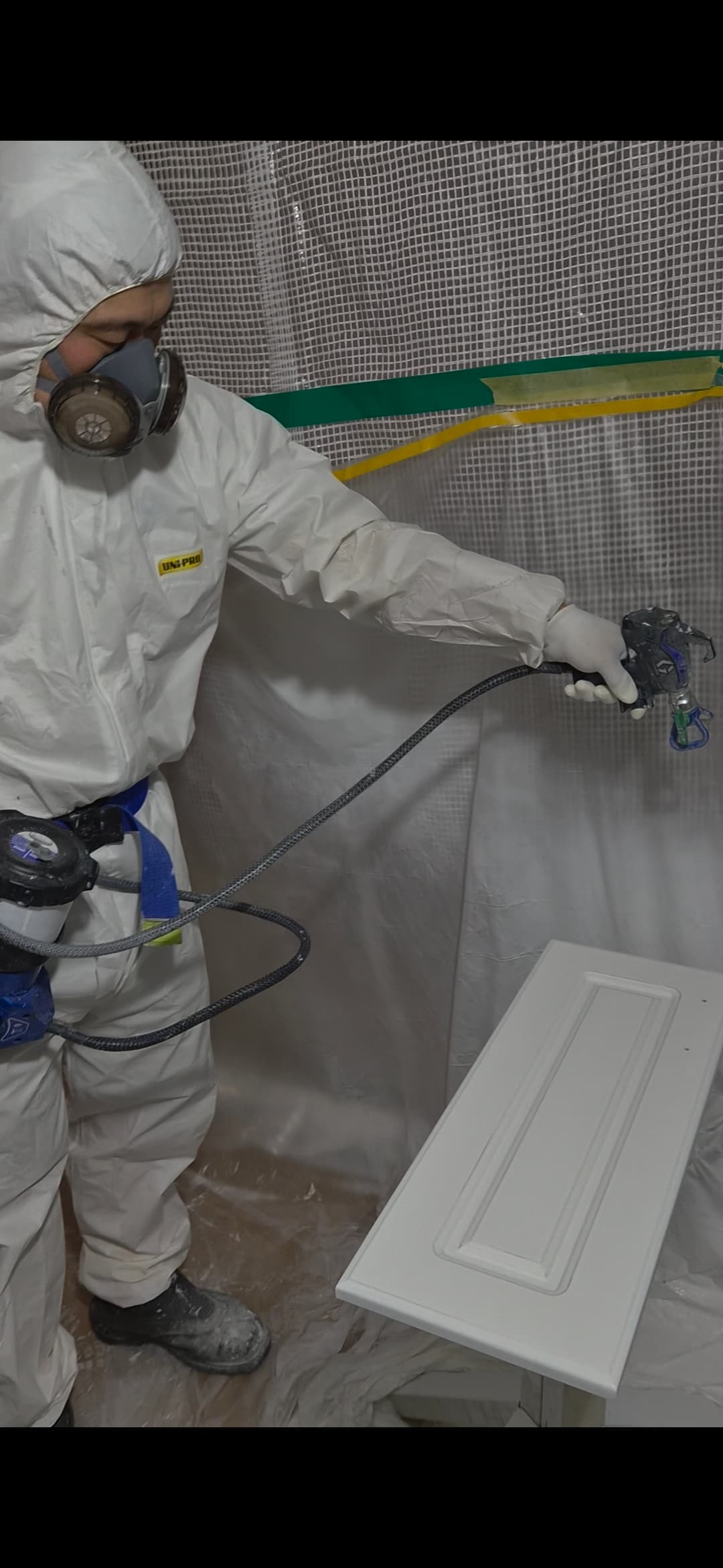 Company-provided photograph of a worker spray-painting a cabinet door in a booth.